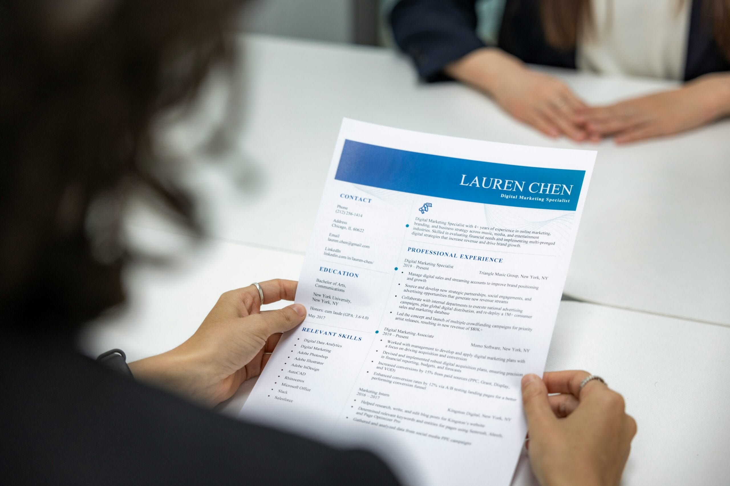 a woman is reading a resume at a table How to Answer Tell Me About Yourself in an Interview