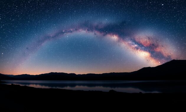 A serene night sky filled with a multitude of stars, showcasing a vibrant Milky Way arching gracefully across the horizon. In the foreground, a silhouetted landscape features gentle rolling hills, while a calm lake mirrors the celestial scene, adding an ethereal quality. The middle ground incorporates a few scattered rocks illuminated subtly by soft moonlight, enhancing the depth. The overall composition uses a wide-angle perspective to emphasize the expansive sky. The color palette reflects realistic, natural nighttime hues with deep blues, soft purples, and twinkling whites, showcasing a perfect example of white balance in astrophotography. The mood is tranquil and awe-inspiring, inviting viewers to immerse themselves in the beauty of a true night sky. A serene night sky filled with a multitude of stars, showcasing a vibrant Milky Way arching gracefully across the horizon. In the foreground, a silhouetted landscape features gentle rolling hills, while a calm lake mirrors the celestial scene, adding an ethereal quality. The middle ground incorporates a few scattered rocks illuminated subtly by soft moonlight, enhancing the depth. The overall composition uses a wide-angle perspective to emphasize the expansive sky. The color palette reflects realistic, natural nighttime hues with deep blues, soft purples, and twinkling whites, showcasing a perfect example of white balance in astrophotography. The mood is tranquil and awe-inspiring, inviting viewers to immerse themselves in the beauty of a true night sky.